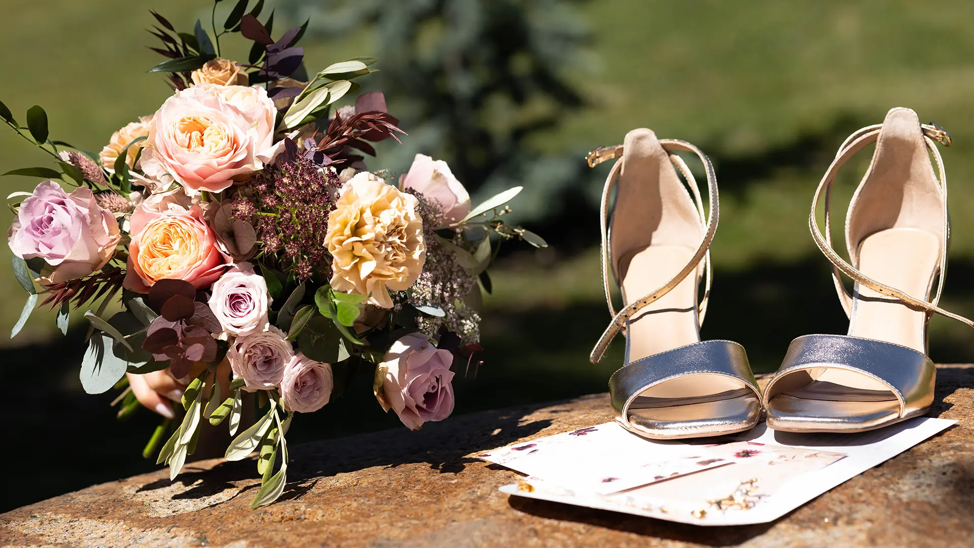 Détails de mariage avec un bouquet de roses poudrées et des chaussures à talons dorées posées sur une pierre