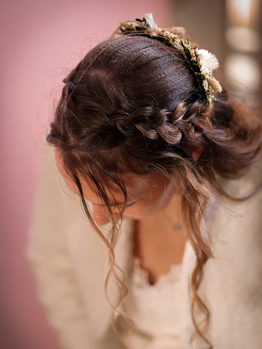 Gros plan sur la coiffure tressée de la mariée ornée d'un accessoire en fleurs séchées