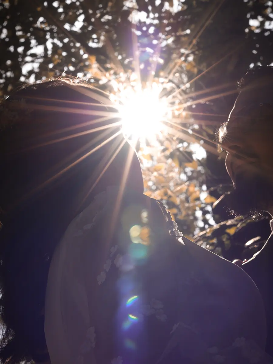 Portrait romantique des mariés en contre-jour avec un rayon de soleil perçant à travers les feuillages
