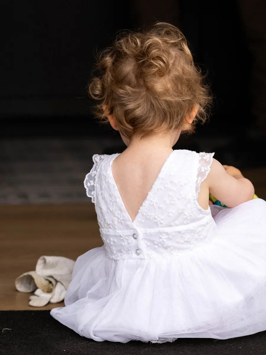 Portrait de dos d'une petite fille aux cheveux bouclés portant une robe blanche en dentelle