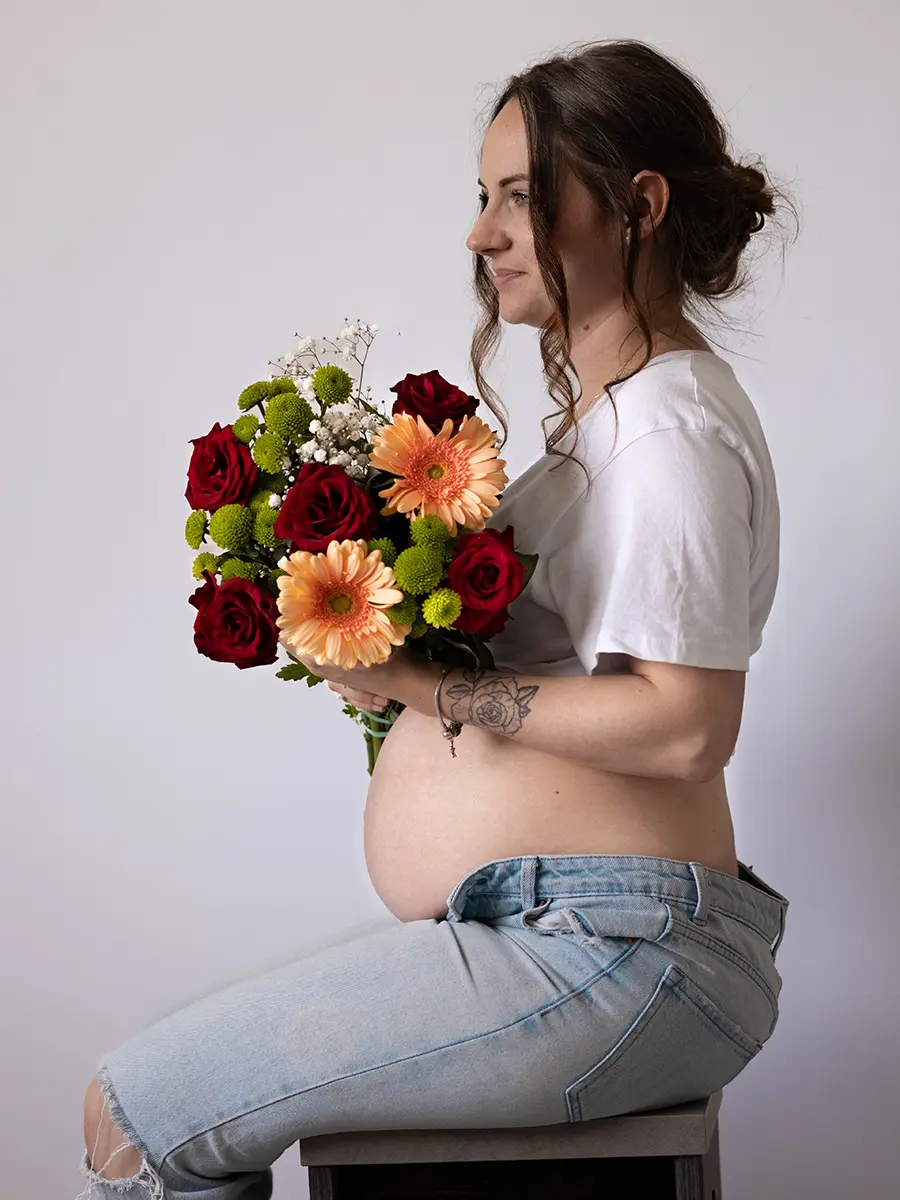 Une femme enceinte de profil tenant un bouquet de fleurs colorées, mettant en valeur son ventre rond