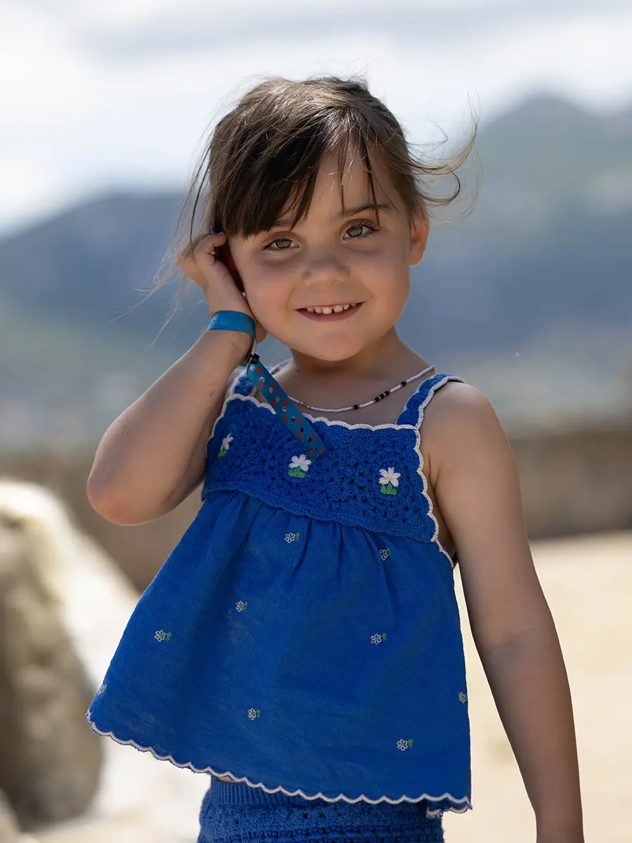 Portrait naturel d'une petite fille souriante vêtue de bleu avec un paysage montagneux en arrière-plan
