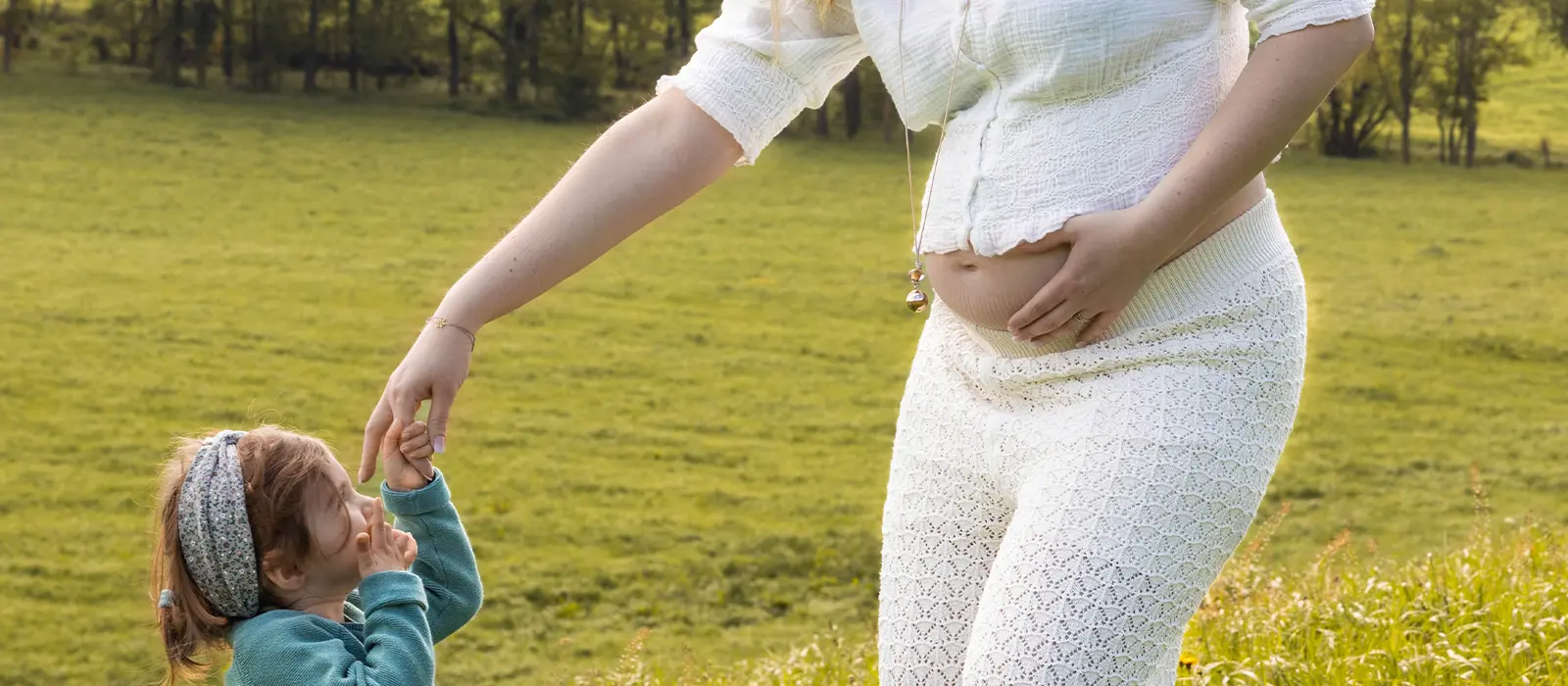 Une femme enceinte en tenue blanche jouant avec sa petite fille dans une prairie verdoyante