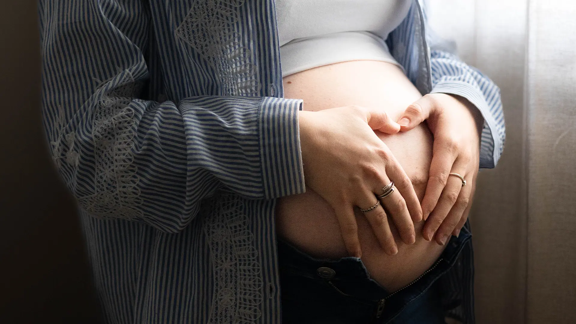 Gros plan sur les mains d'une future maman formant un cœur sur son ventre rond
